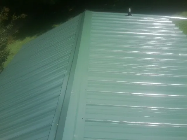 New green metal panels meeting at the ridge of a roof — Flat Roof Repair work by our crew in Dexter