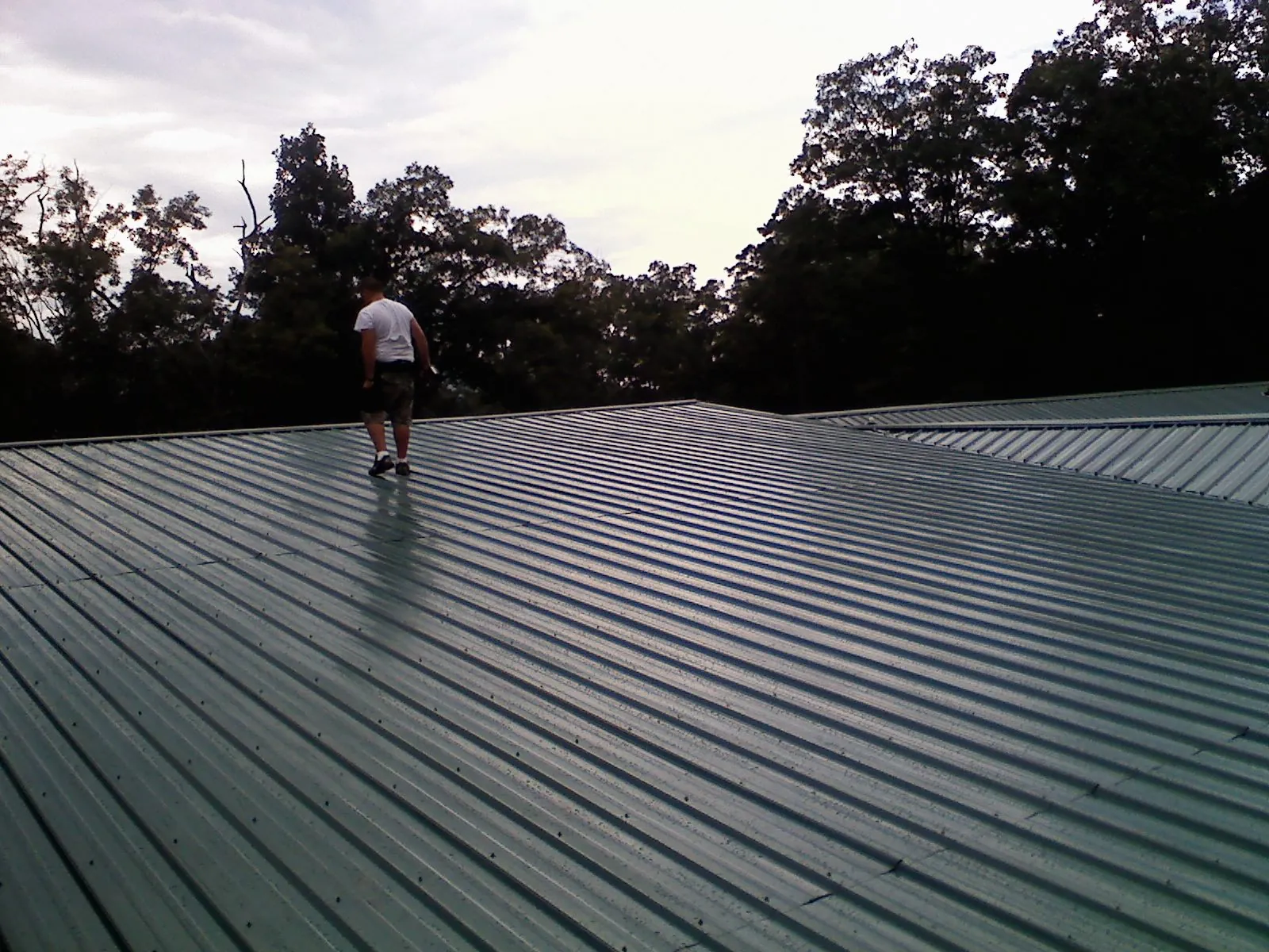 Roofer walking a wide expanse of new green metal roofing in Dexter
